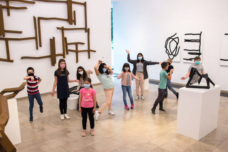 Die Kinder aus der Kunstwerkstatt stehen vor den Skulpturen im Museum und machen Tanzbewegungen