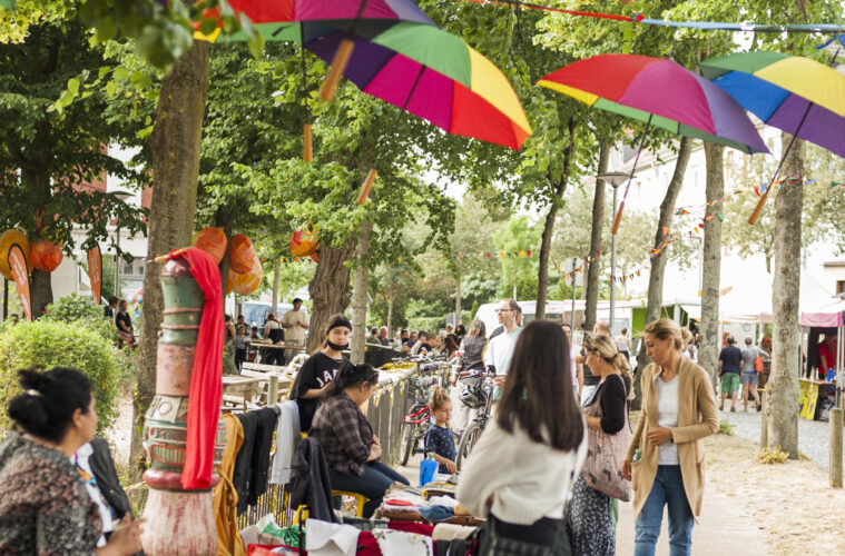 Bild vom Mikrofestival auf dem Liegnitzplatz. In den Bäumen hängen bunte Regenschirme
