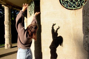 Eine Person macht mit Ihrem Körper und der Sonne ein Schattenspiel vor einer Hauswand