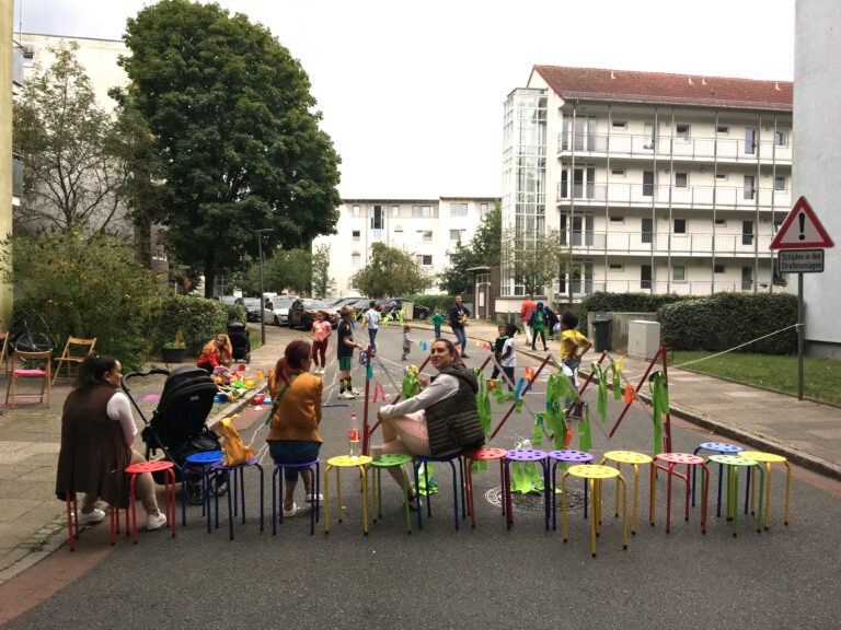Die Spielstrasse wurde am Kunskiosk in der Dirschauer Straße eröffnet. Zu sehen sind Nachbarinnen und Kinder die Spielen.