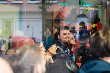 Ein Blick durch die Glasscheibe des Zweiradladen Lindenhof. Drinnen hören Gäste eine Geschichte im Rahmen des internationalen Erzählfestival Feuerspuren. Ein Mann guckt nach draußen und lächelt