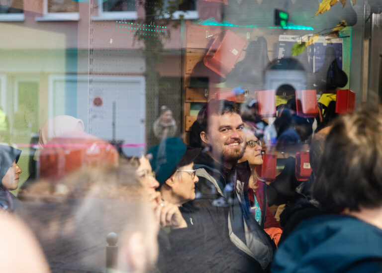 Ein Blick durch die Glasscheibe des Zweiradladen Lindenhof. Drinnen hören Gäste eine Geschichte im Rahmen des internationalen Erzählfestival Feuerspuren. Ein Mann guckt nach draußen und lächelt